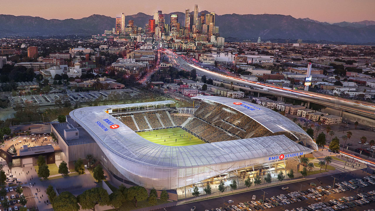 Aerial view of BMO Stadium at dusk with the downtown Los Angeles skyline behind it
